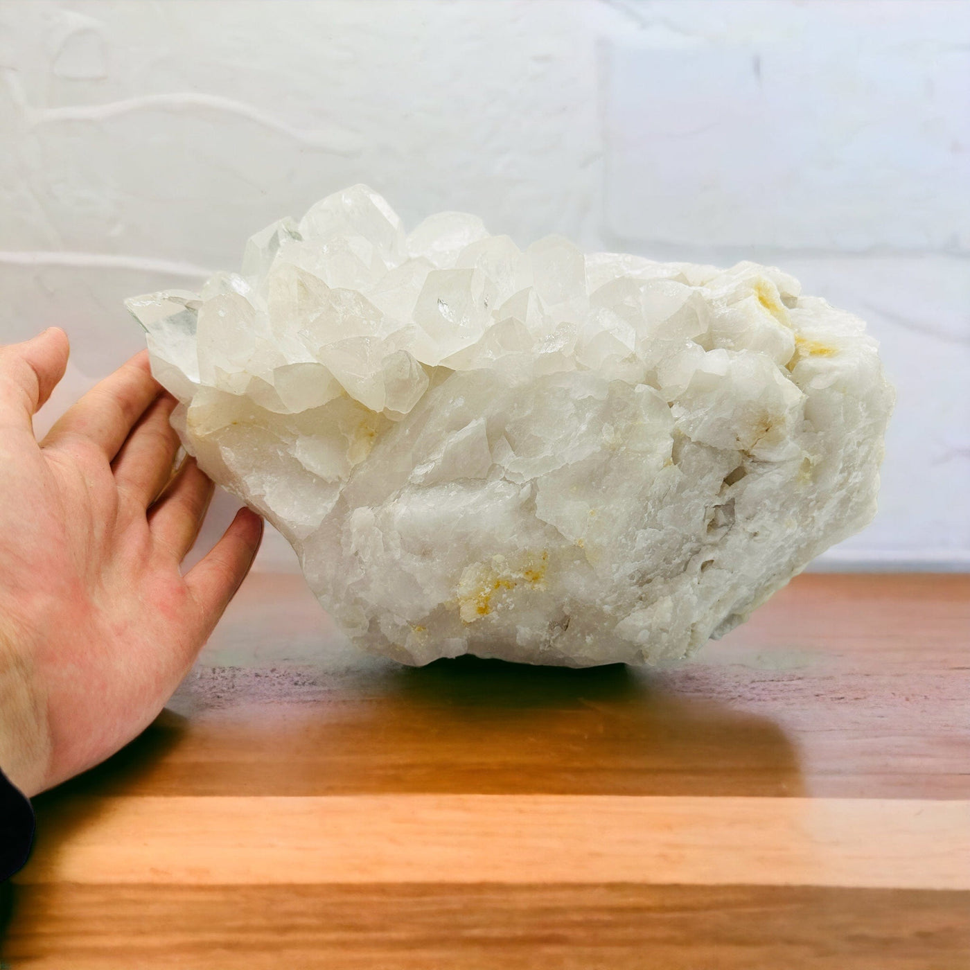 hand next to crystal quartz cluster on a table