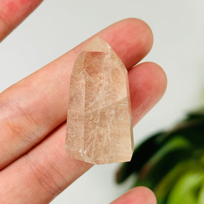 fingers holding up rutilated quartz point with decorations in the background