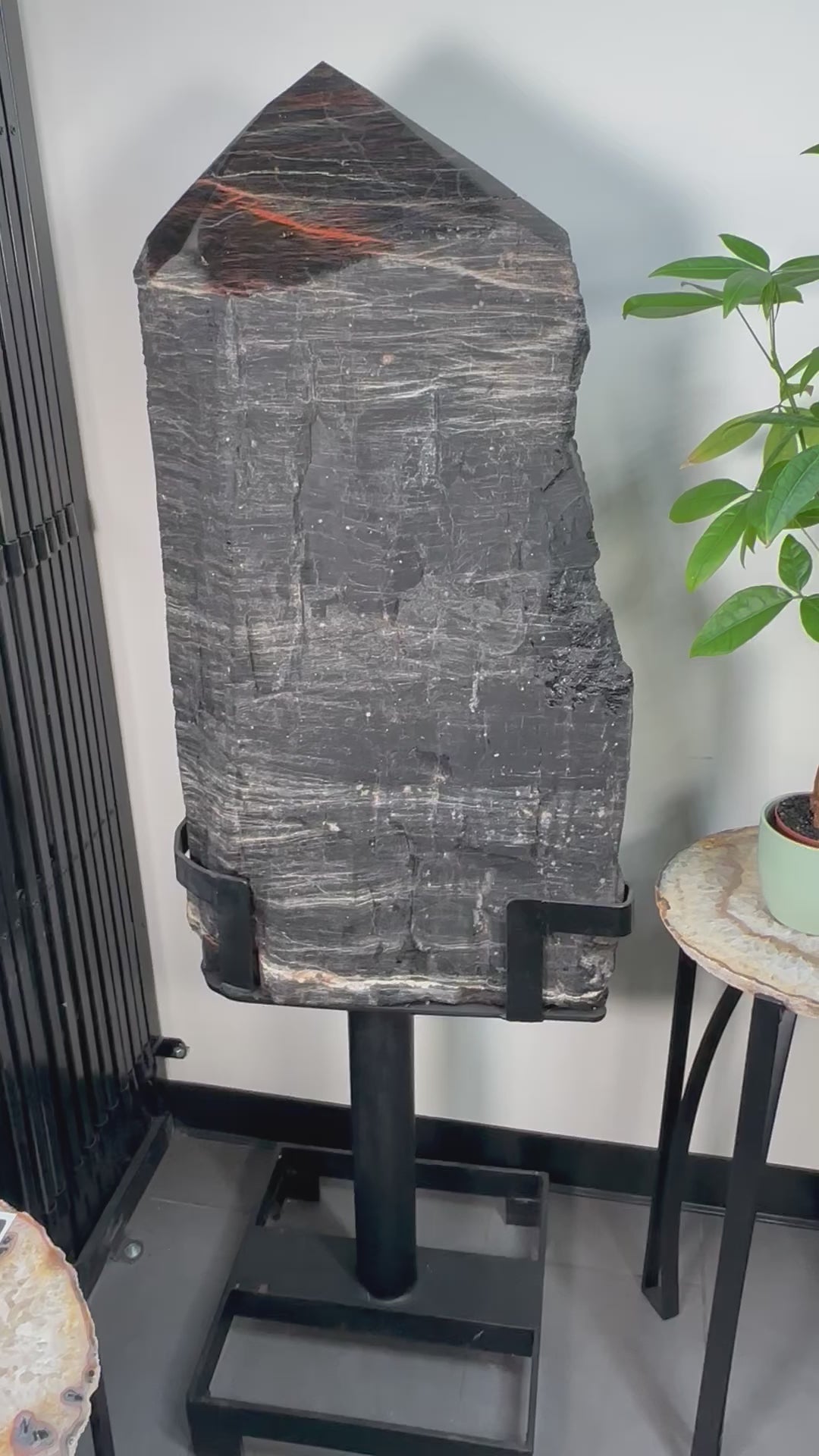 Video of a large black tourmaline point on a black metal stand.  It is black with red veining on the top.
