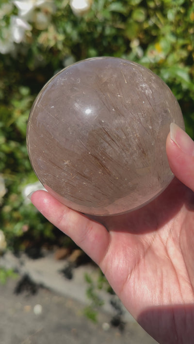 Rutilated Quartz Crystal Sphere - One-of-a-Kind video of sphere in hand swiveling sphere around to show glint of rutile