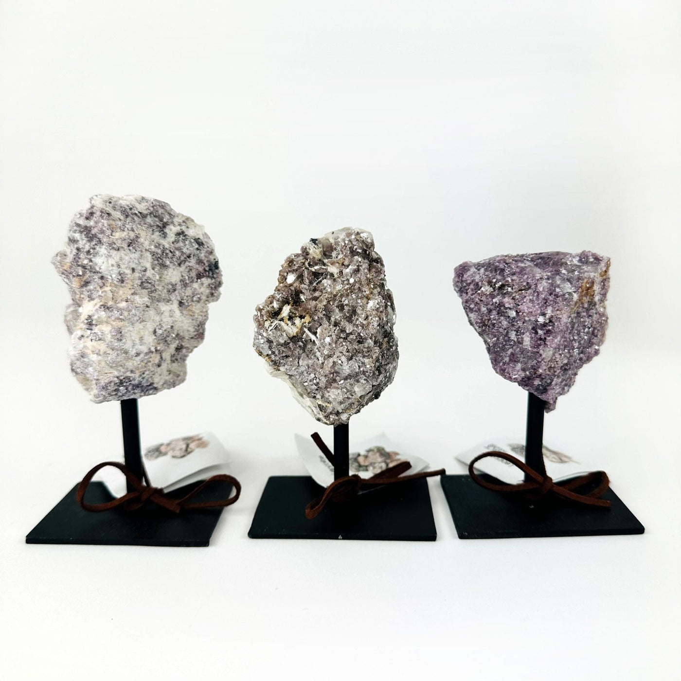 3 Lepidolite stones on Metal Stands in a row on a table