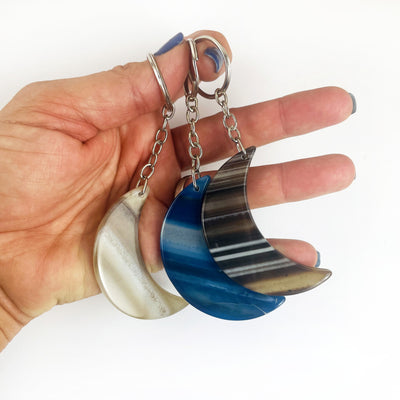 Crescent Moon Agate Key Chains in black, blue and natural agate in a hand for size reference
