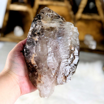 hand holding up Smokey Quartz raw Point with decorations in the background