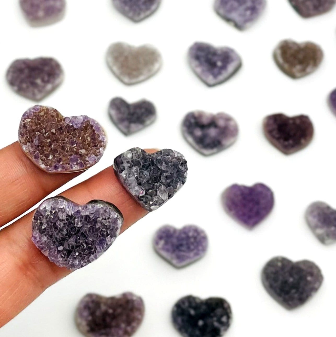 Assorted shades of amethyst hearts in light purple, dark purple, black, purple with brown and other variety on a white background.