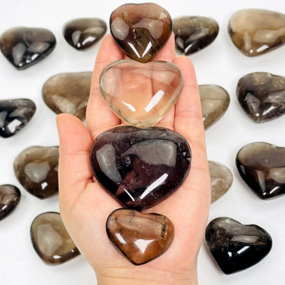 four smokey quartz polished hearts in hand for size reference and possible variations with many others in background