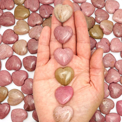 Hand holding up 6 Rhodonite Heart Shaped Stones with more scattered in the background