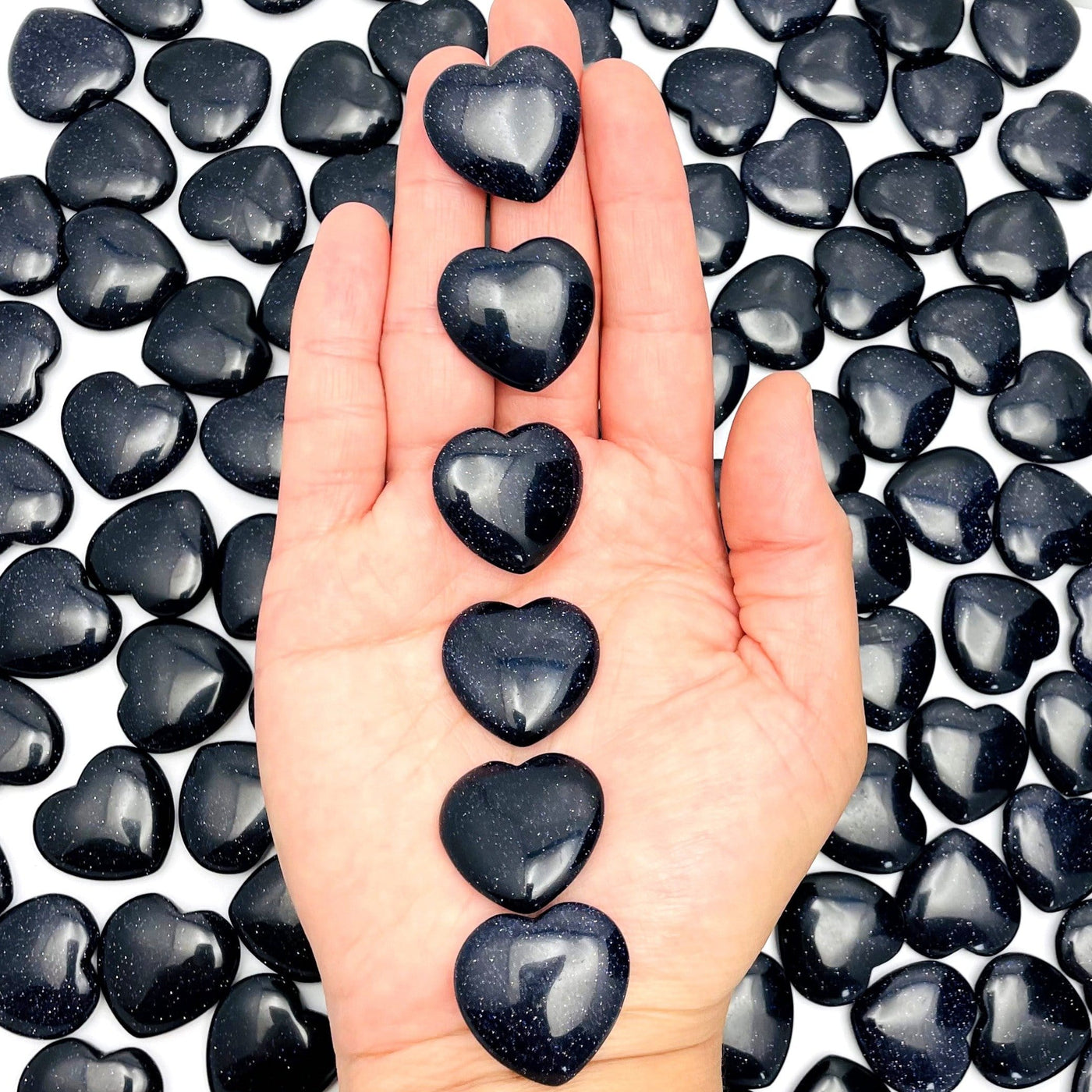 Dark Blue Goldstone Hearts in Hand on Multiple Dark Blue Goldstone Hearts Background.