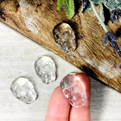 2 fingers holding up crystal skull cabochon with 3 others on a table with decorations