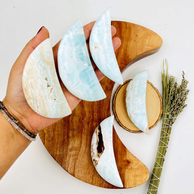 3 blue argonite moons in a woman's hand and two more set on wood in the background.