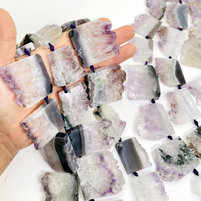 Hand holding up amethyst slice beads with others ion white background