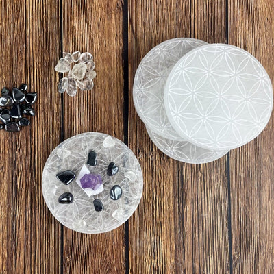overhead view of selenite round plate engraved with flower of life with charging stones and others stacked on display