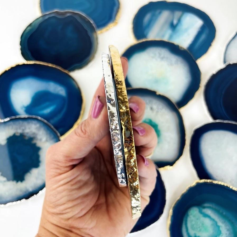 A hand holding 2 Teal Agate coasters with a silver , gold electroplated edge on its side to see the view of the plating , Slices measure about 3.5-5"
