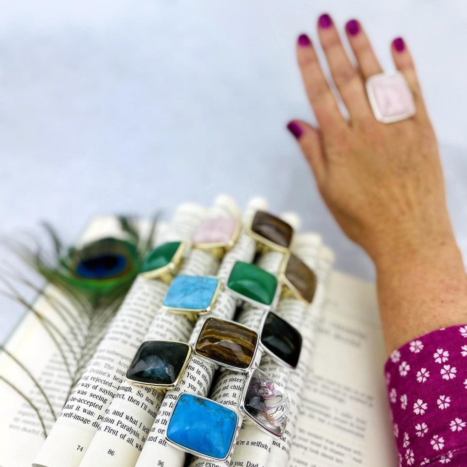 angled shot of book with folded pages displaying stone rings with hand wearing one blurred in the background