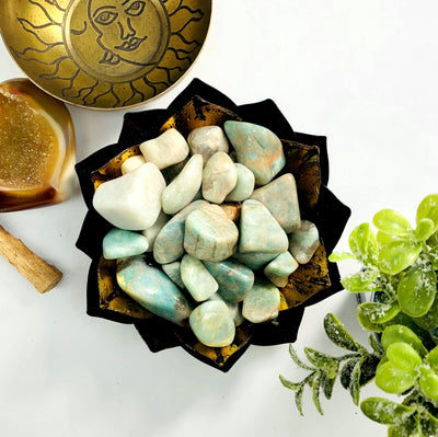 amazonite tumbled stones displayed on a copper bowl next to a plant and another crystal.