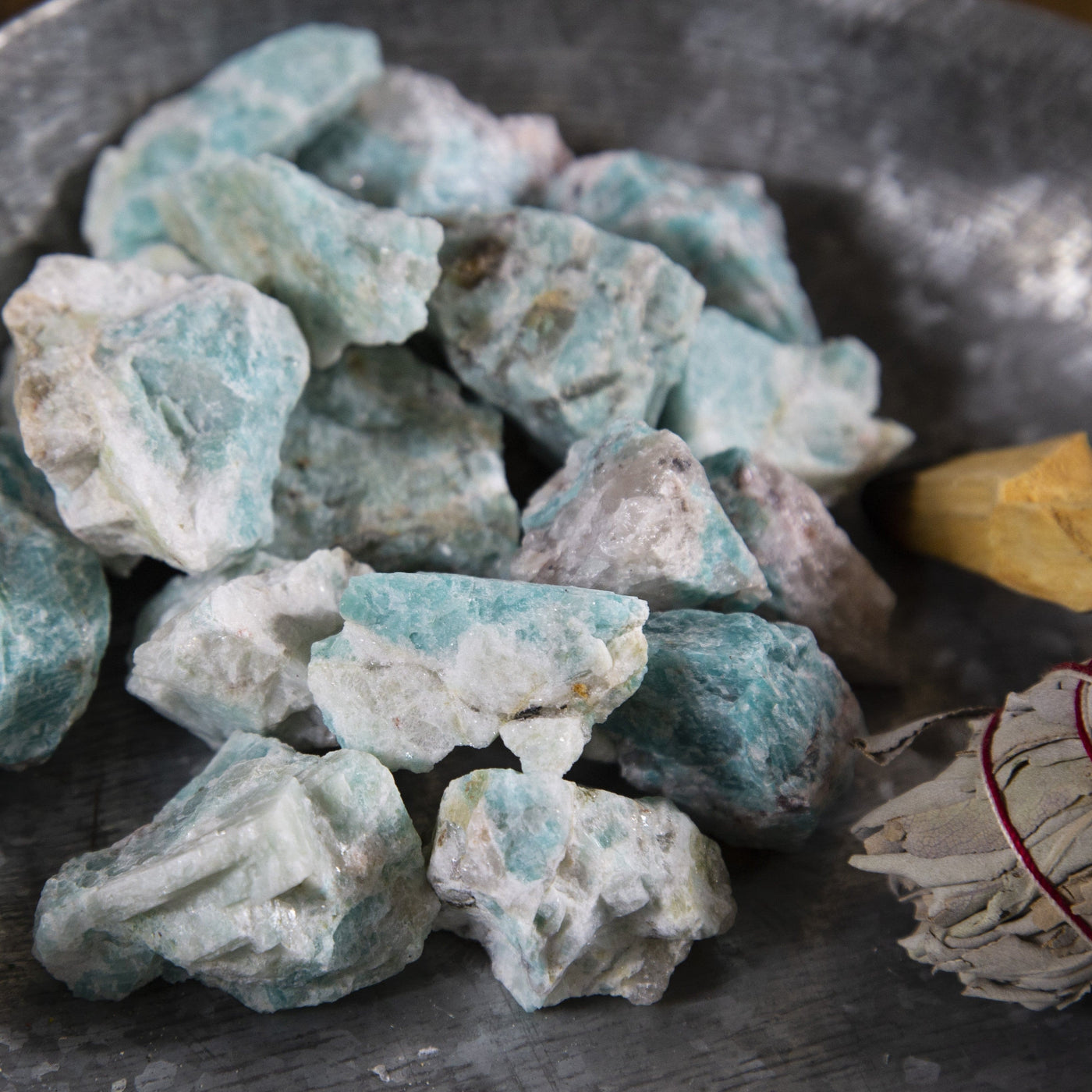 Picture of amazonite chunks being displayed on an offering bowl next to some sage and palo santo.