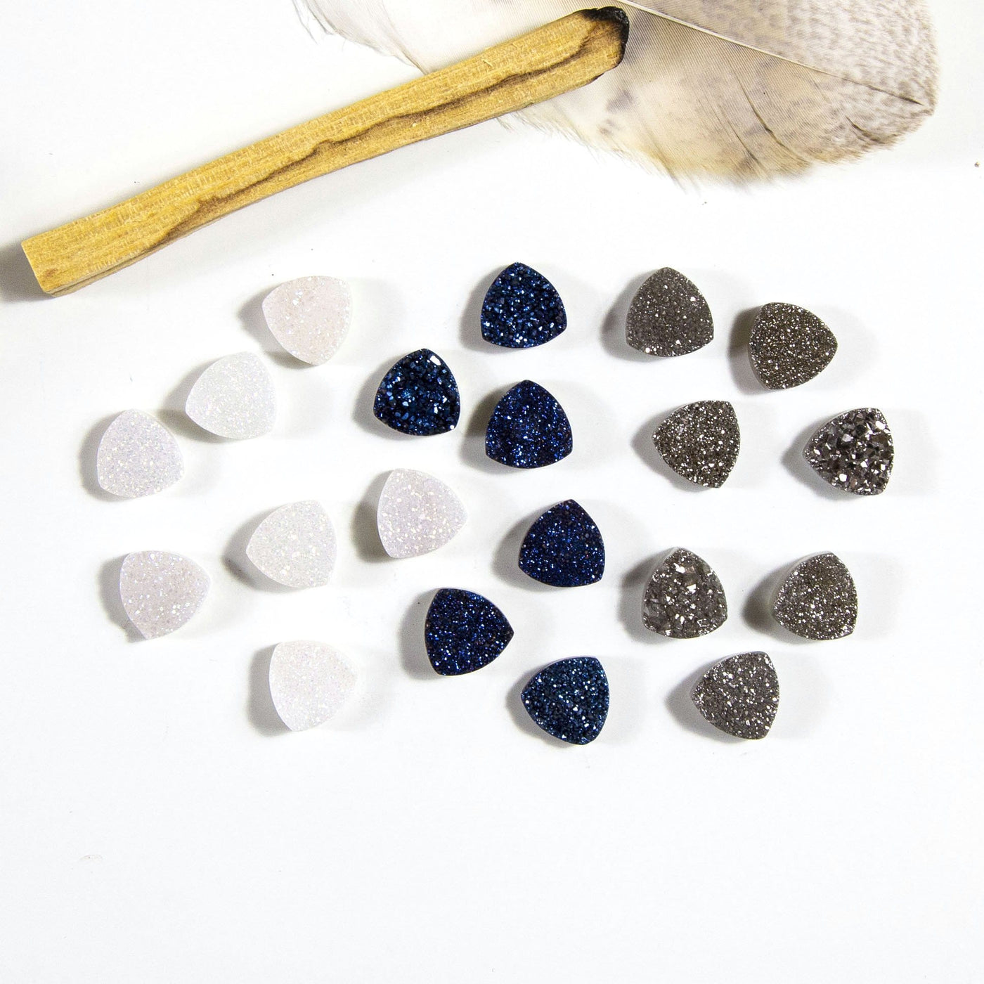 multiple triangle shaped druzy cabochons displayed on white background to show they come in white mystic blue and platinum each with various characteristics