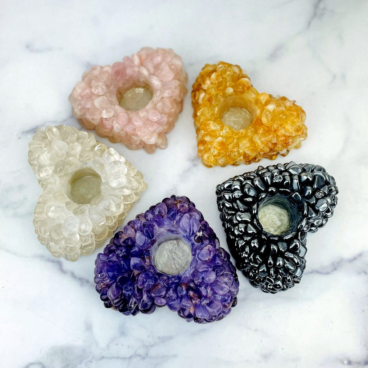 A photo of all the available glued tumbled stone heart candle holders.  Pictured is rose quartz, citrine, crystal quartz, amethyst and hematite.