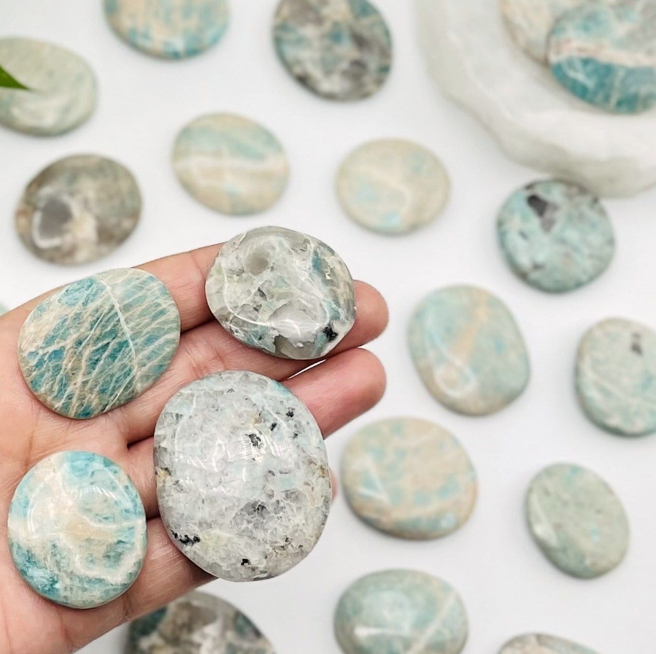 amazonite polished stones being held for size reference, other stones are also in the back ground. 