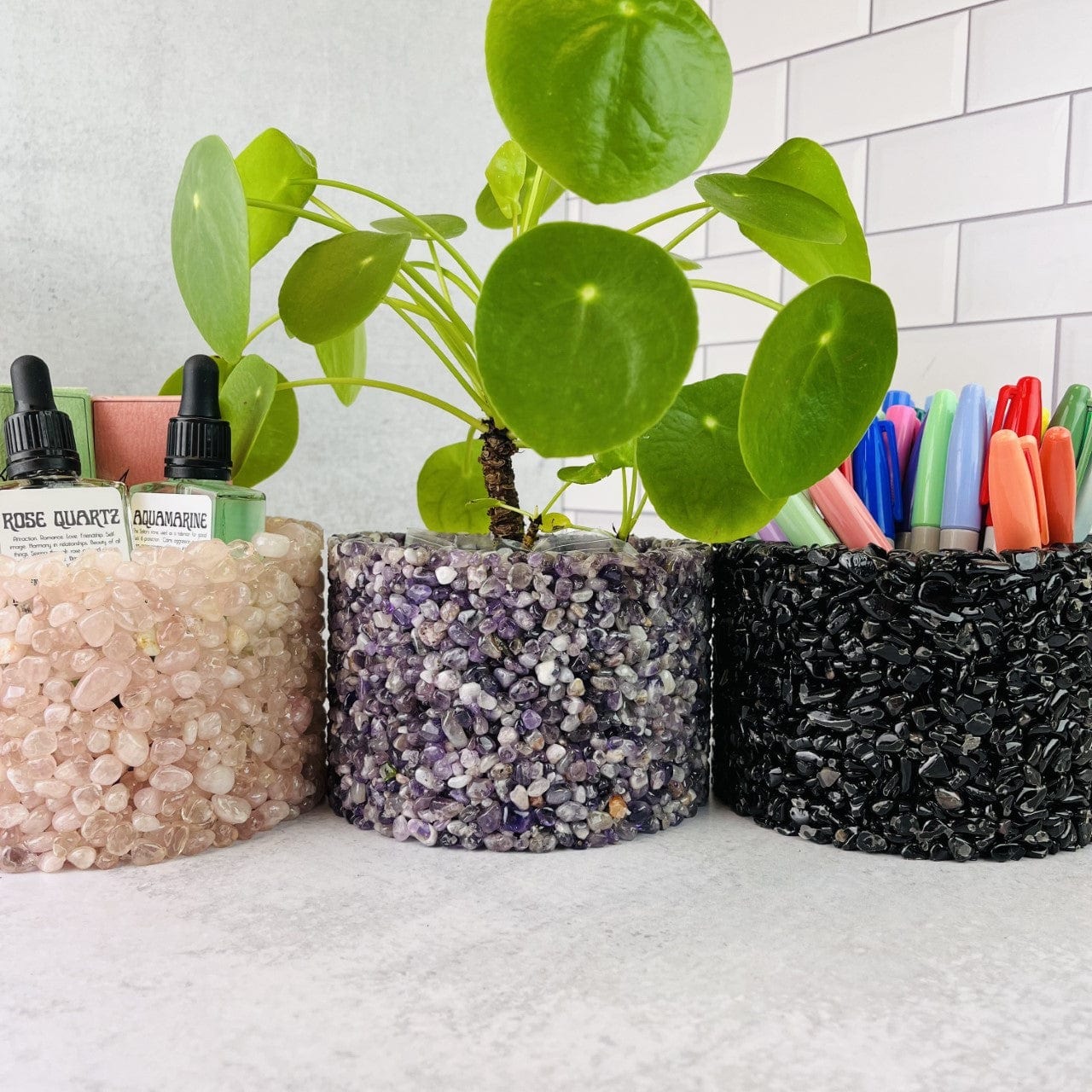 3 Tumbled Stone Pot/Holders #4 up close, a rose quartz holder holding oil bottles, the amethyst one holding a plant and the tourmaline one holding pens