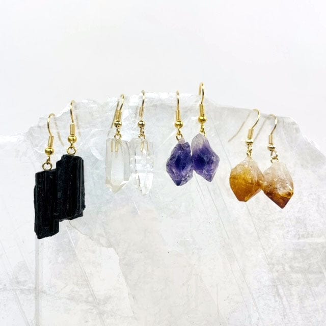Black tourmaline earrings, crystal point earrings, amethyst point earrings and citrine point earrings.  All have gold ear wires and are hanging from a selenite slab.