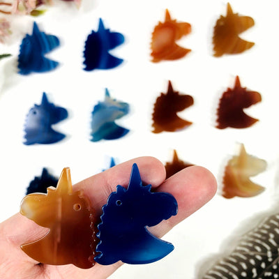 Blue and natural agate unicorn heads being displayed on a white back ground. They are also being held for size reference.