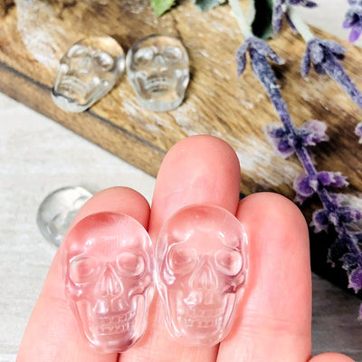 2 fingers holding up crystal skull cabochon with 3 others on a table with decorations