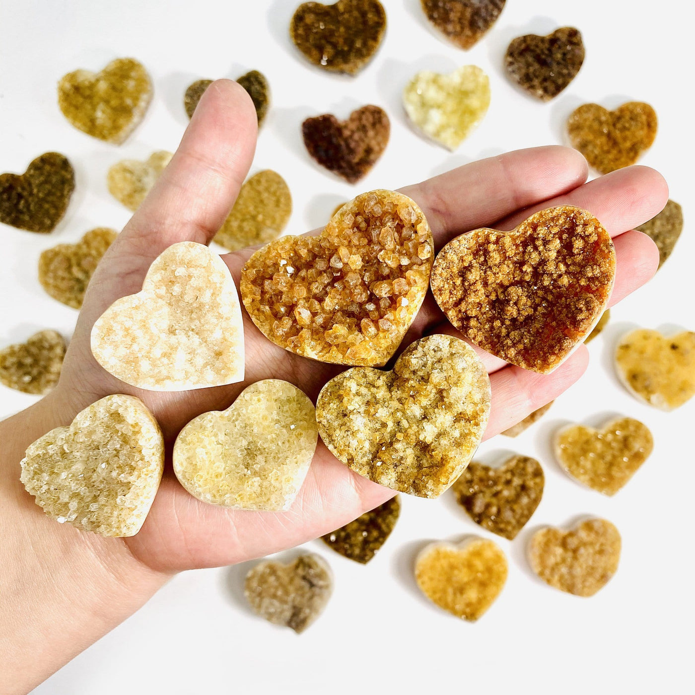 hand holding up 6 Citrine Cluster Druzy Hearts with others in the background