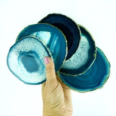 A hand holding 5 Teal Agate coasters with a silver , gold electroplated edge Slices measure about 3.5-5"