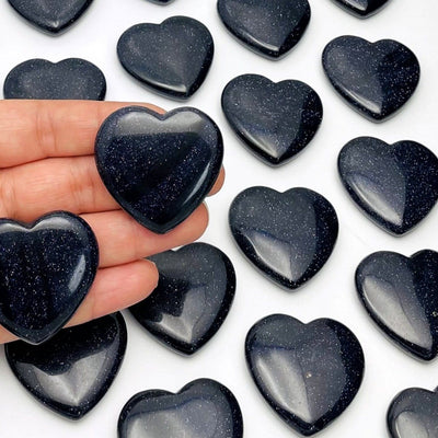 2 Dark Blue Goldstone Hearts in Hand on Dark Blue Goldstone and White Background.