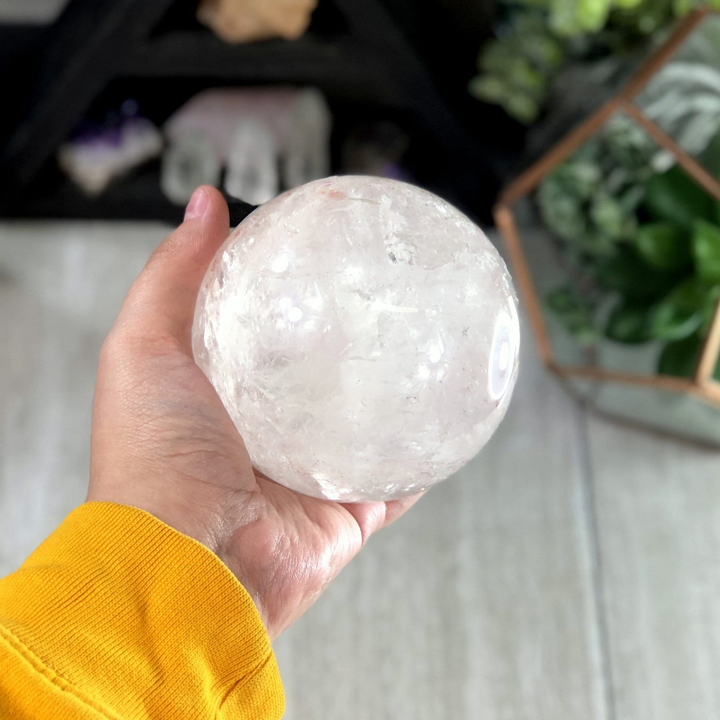 hand holding up crystal quartz polished sphere with decorations in the background