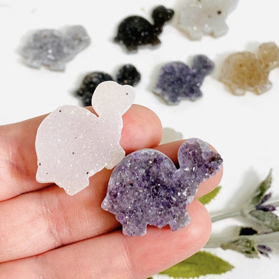 hand holding up 2 druzy turtle cabochons with decorations blurred in the background