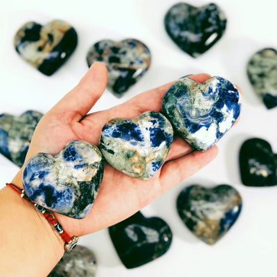 three sodalite heart shaped stones in hand for size reference with many others in background