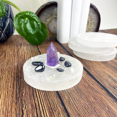 angled view of selenite round plate engraved with flower of life with charging stones for thickness and others in background display