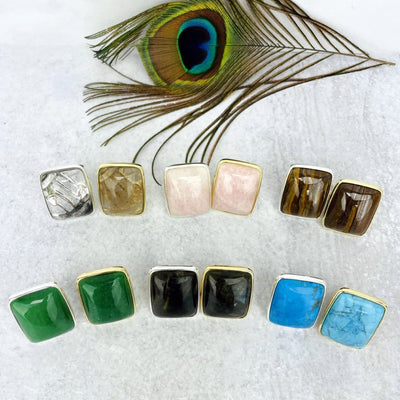 top view of various stone rings in gold and silver in front of peacock feather