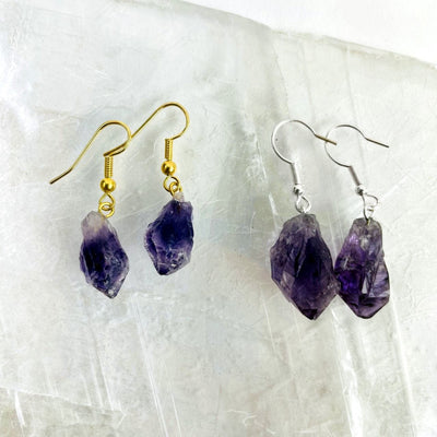 Close up of amethyst point earrings in gold and silver plated on a selenite slab.