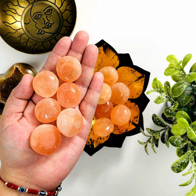 Orange selenite spheres in a hand with more under it in a lotus candle holder.