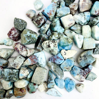 Larimar Tumbled Stones are spread out  to show various colors textures natural inclusions sizes shapes