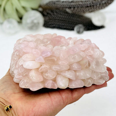 Hand holding Rose Quartz Tumbled stone Heart Candle Holder showing side of it with decorations blurred in the background