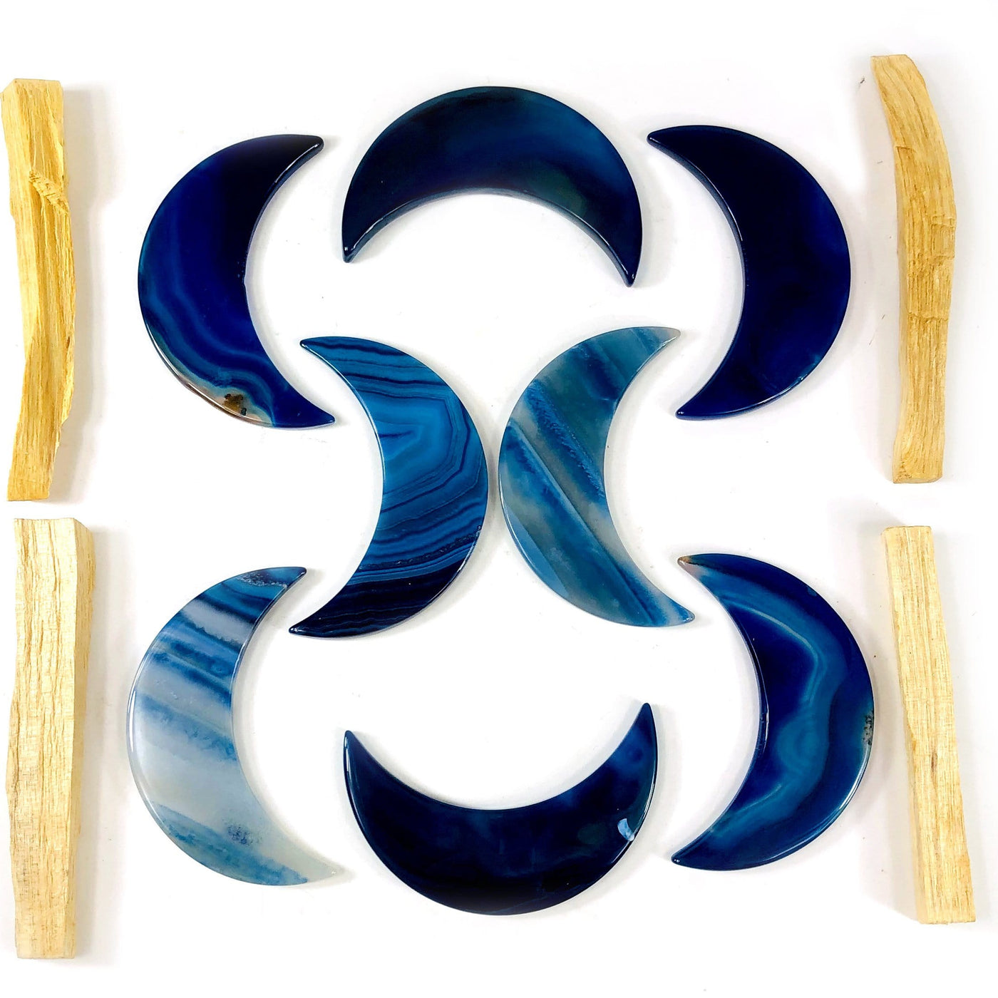 Eight blue agate moons displayed on a white surface next to palo santo.