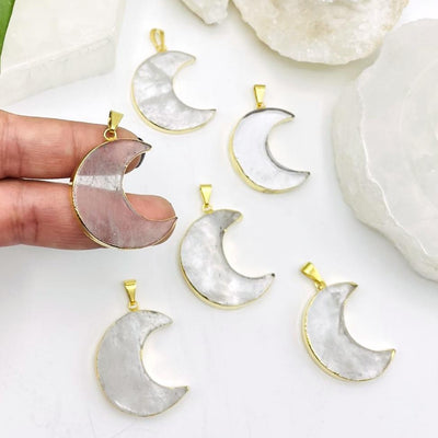 2 fingers holding up crystal quartz half moon pendant with 5 more in the background