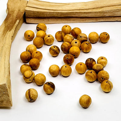 multiple palo santo beads with a drill hole that goes through the whole bead displayed on a white background 