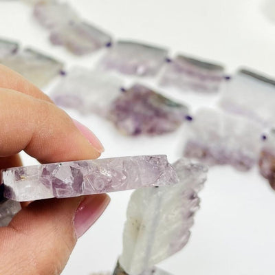 Hand holding amethyst slice bead to show thickness of bead with others blurred on white background