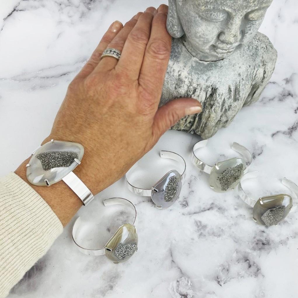 hand wearing titanium druzy angel aura agate bracelet with 4 others and a Buddha statue in the background