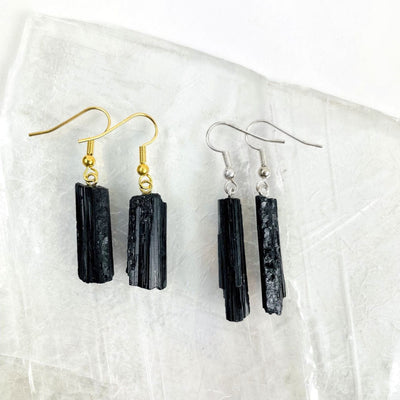 Close up of black tourmaline rod earrings gold and silver plated on a selenite slab