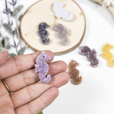 hand holding up druzy seahorse cabochon for size reference with others blurred in the background with decorations