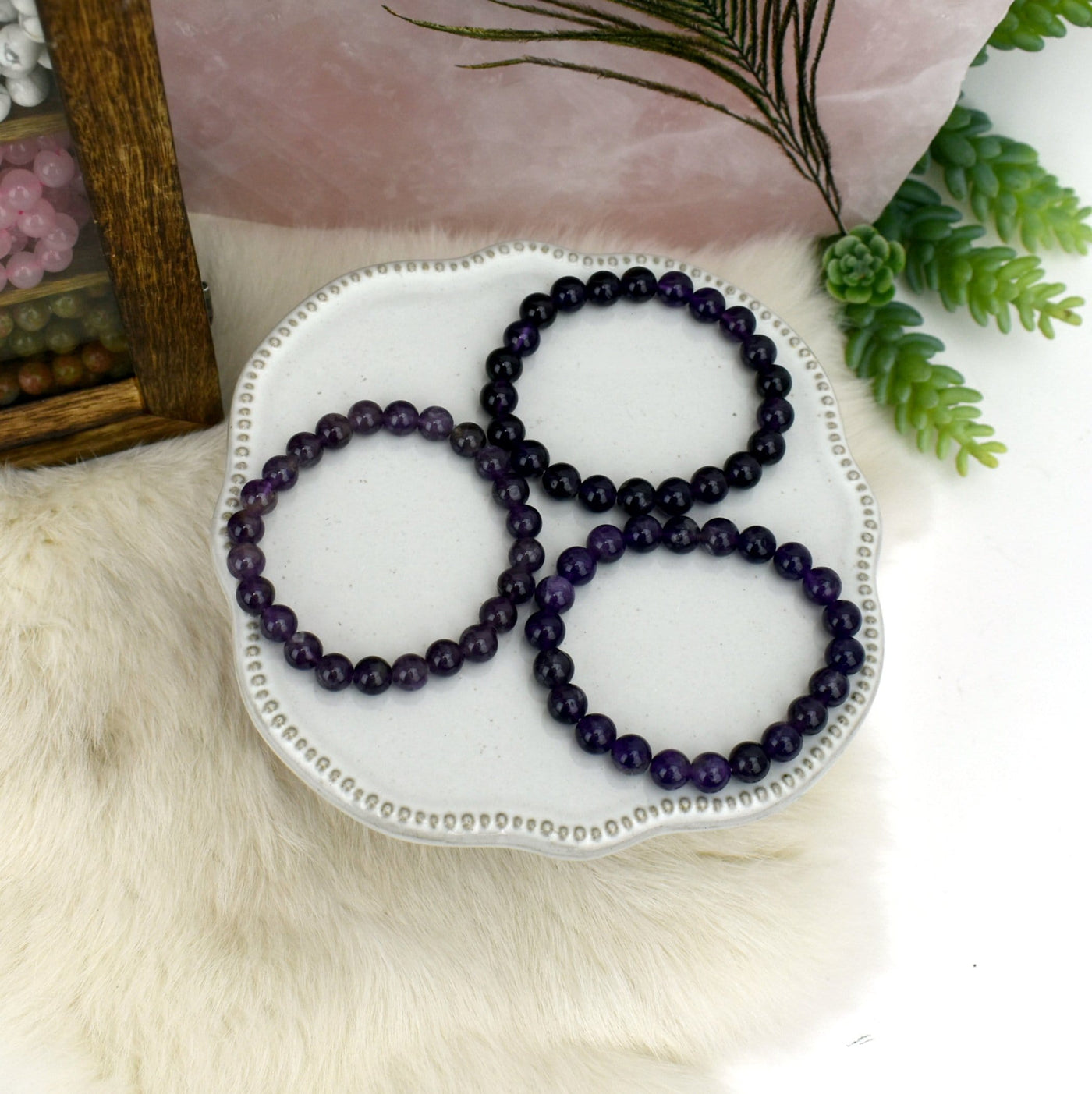 3 Amethyst Round Bead Bracelets on white plate with decorations in the background