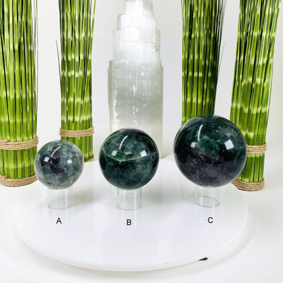 Picture of all 3 rainbow fluorite spheres lined up next to each other, displayed on a white background. 