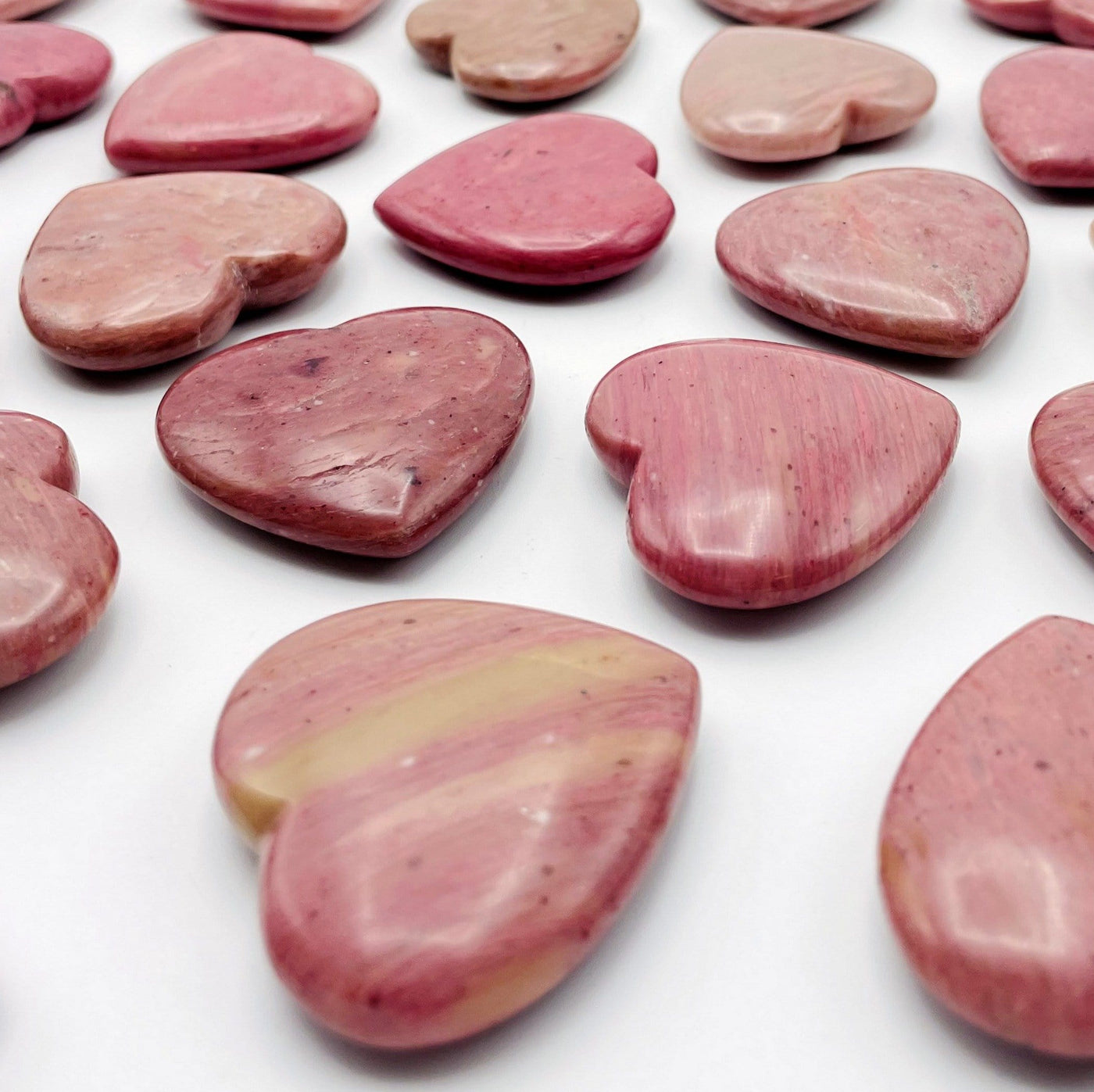 Angled view of Rhodonite Heart Shaped Stones scattered on white background
