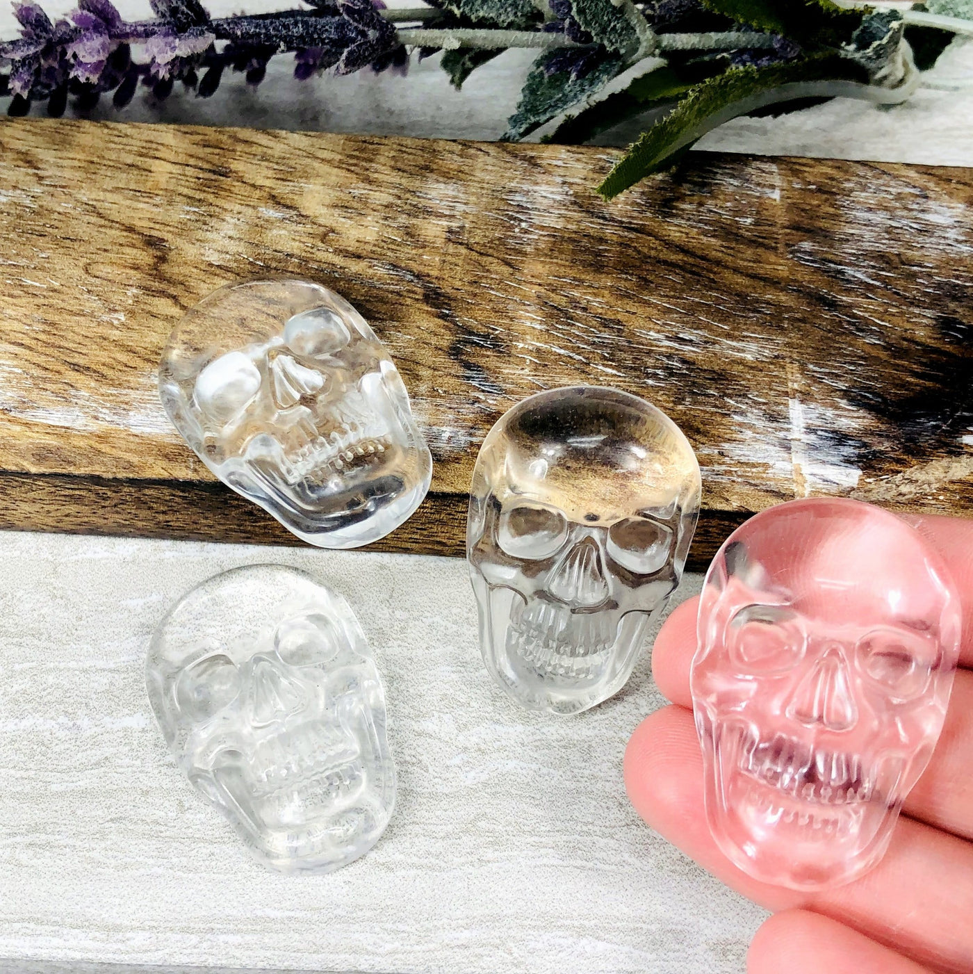 hand holding up crystal quartz crystal skull cabochons with 3 others in the background with decorations