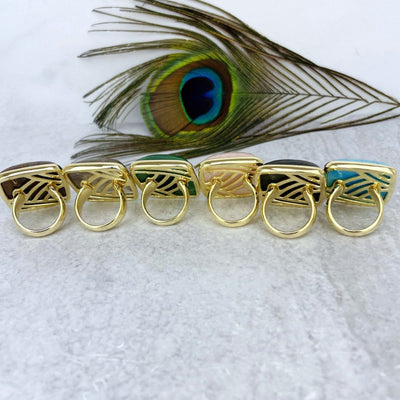 back view of gold stone rings in front of peacock feather